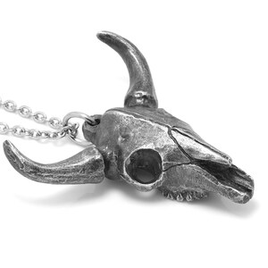 May include: A silver necklace with a detailed pewter bull skull pendant. The pendant has a textured surface and realistic features.