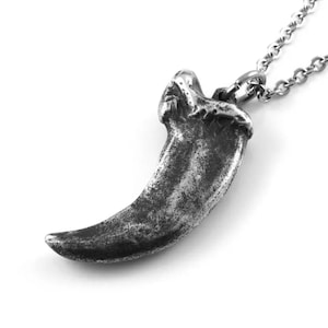 May include: A silver claw pendant necklace. The pendant is detailed and realistic, with a textured surface. The necklace is made of a silver chain.