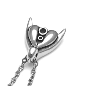 Puede incluir: Un collar con un colgante de plata en forma de coraz&oacute;n y dos cuernos. El colgante tiene un dise&ntilde;o detallado con un peque&ntilde;o c&iacute;rculo en el centro.