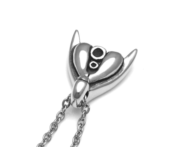 Puede incluir: Un collar con un colgante de plata en forma de coraz&oacute;n y dos cuernos. El colgante tiene un dise&ntilde;o detallado con un peque&ntilde;o c&iacute;rculo en el centro.