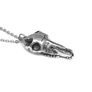 May include: A silver necklace with a detailed skull pendant. The skull is of a horse or other animal with a long snout.