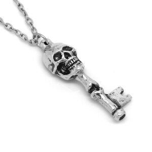 May include: A silver skull key pendant necklace. The skull is detailed with a toothy grin and the key has a traditional design.
