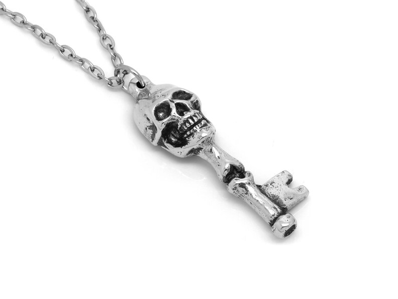 May include: A silver skull key pendant necklace. The skull is detailed with a toothy grin and the key has a traditional design.