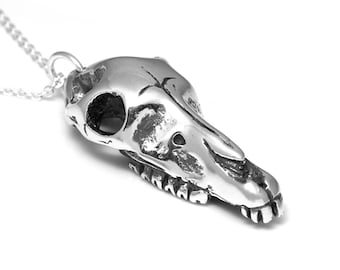 May include: A silver pendant necklace featuring a detailed skull of a small animal, possibly a deer or a goat. The skull is intricately sculpted with visible teeth and eye sockets.