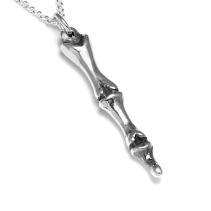 May include: A silver pendant necklace featuring a detailed anatomical bone design. The pendant is shaped like a human finger bone, with a realistic depiction of the joints and bone structure.