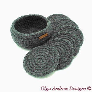 May include: A set of gray crocheted coasters and a matching basket. The coasters are round and arranged next to the basket. The basket has a small, rectangular tag. The text "Olga Andrew Designs" is at the bottom.