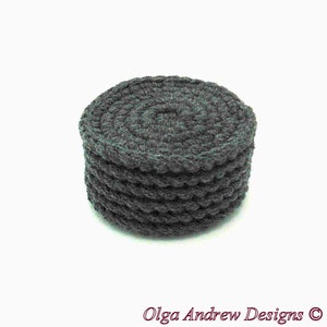 May include: A dark gray, round, crocheted coaster. The coaster is made of thick yarn and has a textured, spiral design on top. The sides have a scalloped edge. The text "Olga Andrew Designs" is at the bottom.
