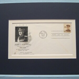 May include: Framed First Day Cover featuring John J. Pershing, an American military leader. The cover includes a portrait, a stamp, and the text "First Day of Issue." The frame is a dark navy blue.