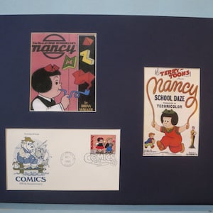May include: A framed collection of Nancy comic book covers and a stamp commemorating the 100th anniversary of comics. The covers feature Nancy in various poses, including one where she is holding a pipe and another where she is jumping rope. The stamp features a cartoon image of two children.