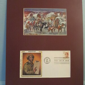 May include: A framed first day of issue stamp featuring Sequoyah, the inventor of the Cherokee syllabary. The stamp is surrounded by a white border and a red mat. The image shows Sequoyah holding a piece of paper with the Cherokee syllabary written on it. The stamp is dated December 27, 1980.