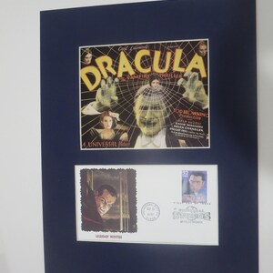 May include: A framed image of a vintage movie poster for the 1931 film "Dracula", featuring a spiderweb and the text "The Vampire Thriller". Below the poster are two stamps, one depicting Bela Lugosi as Dracula and the other a Universal Studios logo.