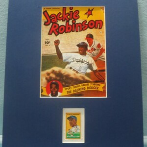May include: A framed image of a vintage comic book cover featuring Jackie Robinson, a baseball player for the Brooklyn Dodgers. The cover is red, white, and blue with the text "Jackie Robinson" in large, bold letters. The image also includes a smaller, framed image of a baseball card featuring Jackie Robinson.