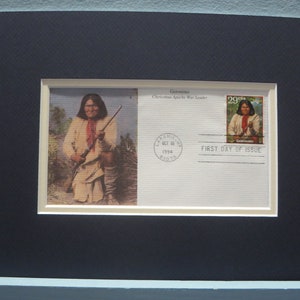Könnte beinhalten: Ein gerahmter Ersttagsbrief für die Geronimo-Briefmarke. Der Umschlag zeigt ein Bild von Geronimo, einem Chiricahua-Apache-Kriegerführer, der ein Gewehr hält. Die Briefmarke befindet sich in der oberen rechten Ecke des Umschlags und zeigt ein Porträt von Geronimo. Der Umschlag trägt außerdem einen Poststempel vom 18. Oktober 1994 aus der Stadt Red Cloud, Nebraska.