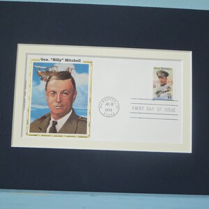 May include: A framed first day of issue envelope featuring a portrait of General "Billy" Mitchell, a pioneer of American air power. The envelope is cream colored with a gold border and includes a stamp with a portrait of General Mitchell in uniform. The text "First Day of Issue" is printed on the envelope.