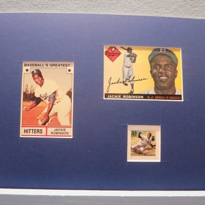 May include: A blue mat with three baseball cards featuring Jackie Robinson. The cards are from the "Baseball's Greatest" series and show Robinson in different poses. The cards are framed and mounted on the mat.