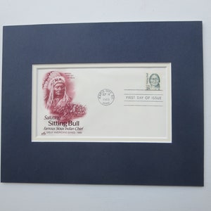 Peut inclure: Une enveloppe encadrée représentant Sitting Bull, célèbre chef sioux, avec l'inscription « Saluting Sitting Bull ». L'enveloppe est datée du 14 septembre 1989 et comprend un timbre avec le portrait d'une femme. Le cadre est bleu foncé.