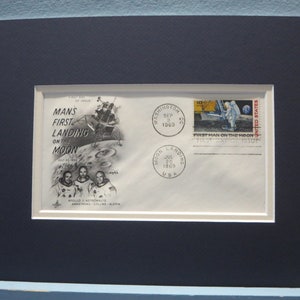 May include: A framed first day of issue envelope commemorating the first manned landing on the moon. The envelope features a black and white illustration of the lunar module landing on the moon, with three astronauts standing below. The envelope also includes a stamp depicting an astronaut walking on the moon, with the text "First Man on the Moon".