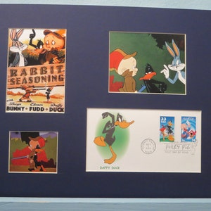 Puede incluir: Una impresión enmarcada con cuatro imágenes de Bugs Bunny, Daffy Duck y Porky Pig de la clásica serie de dibujos animados. La imagen superior izquierda muestra a Bugs Bunny, Daffy Duck y Elmer Fudd con el texto "Rabbit Seasoning" y "Bugs Bunny - Elmer Fudd - Daffy Duck". La imagen superior derecha muestra a Bugs Bunny, Daffy Duck y Elmer Fudd en un entorno de bosque. La imagen inferior izquierda muestra a Elmer Fudd y Daffy Duck en un entorno de bosque. La imagen inferior derecha muestra a Daffy Duck corriendo con un fondo verde y un sello con Porky Pig.