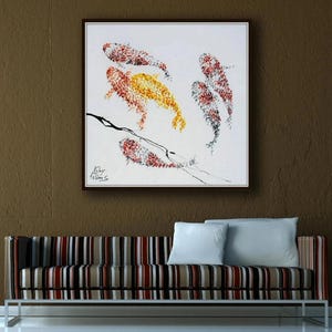 May include: An abstract painting of koi fish in shades of red, yellow, and black on a white background, framed in a dark wood. The artwork hangs above a striped sofa with white pillows.