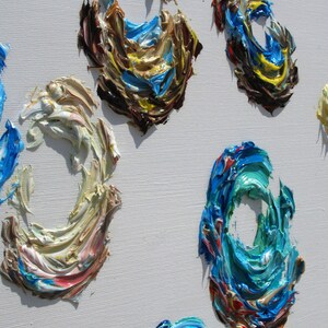 May include: Abstract painting with swirling, textured circles in shades of blue, brown, yellow, white, and red on a white canvas.
