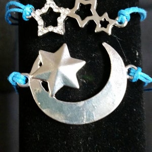 May include: A silver charm bracelet with a crescent moon and stars. The bracelet is made of blue string and has a silver charm with a crescent moon and a star.