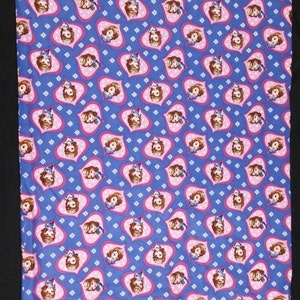 May include: A blue and pink fabric with a repeating pattern of a cartoon princess in a pink heart. The princess has brown hair and is wearing a blue dress.