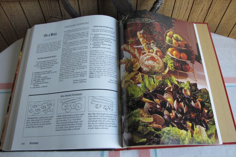 Puede incluir: Libro de cocina abierto con una receta para "On a Roll" de rollos de mantequilla en forma de media luna y una foto de un plato de mariscos con almejas, mejillones y rodajas de lim&oacute;n. El libro de cocina est&aacute; abierto en la secci&oacute;n "Cenas festivas".