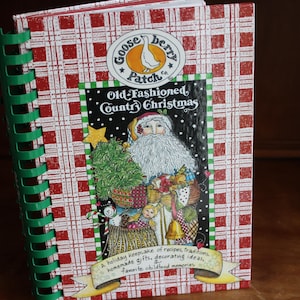 May include: A spiral-bound cookbook titled "Old-Fashioned Country Christmas" by Gooseberry Patch. The cover features a Santa Claus illustration, a Christmas tree, and a banner with text. The background has a red and white plaid pattern.