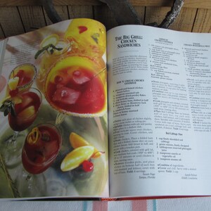Puede incluir: Libro de cocina abierto con una receta para "The Big Grill Chicken Sandwiches". La p&aacute;gina presenta una foto de varios c&oacute;cteles rojos y naranjas con cubitos de hielo y guarniciones. La receta incluye ingredientes como trozos de pi&ntilde;a, col roja y cebollas verdes.