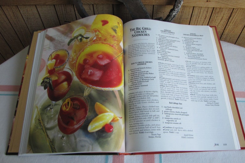 Puede incluir: Libro de cocina abierto con una receta para "The Big Grill Chicken Sandwiches". La p&aacute;gina presenta una foto de varios c&oacute;cteles rojos y naranjas con cubitos de hielo y guarniciones. La receta incluye ingredientes como trozos de pi&ntilde;a, col roja y cebollas verdes.