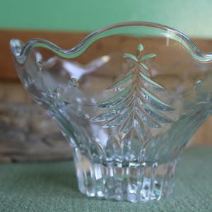 May include: A clear glass bowl with a scalloped rim and a delicate etched design of a Christmas tree. The bowl is perfect for serving snacks or desserts.