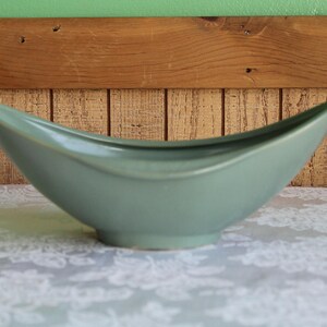 May include: A light blue ceramic bowl with a unique, curved shape. The bowl is sitting on a white, lace-like tablecloth.