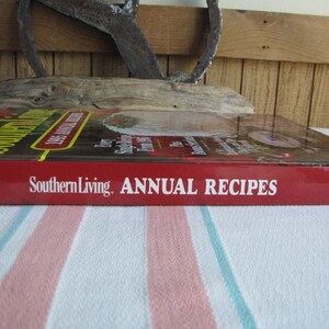 Puede incluir: Un libro de cocina de tapa dura roja titulado "Southern Living Annual Recipes 1995" con el texto "Southern Living Annual Recipes" en el lomo.