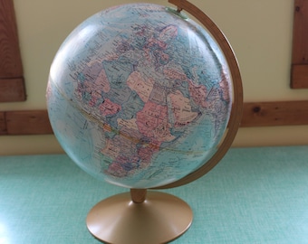 May include: A vintage globe with a light blue ocean and colorful landmasses. The globe is mounted on a gold-colored base and a curved support. The globe is a classic educational tool and decorative item.