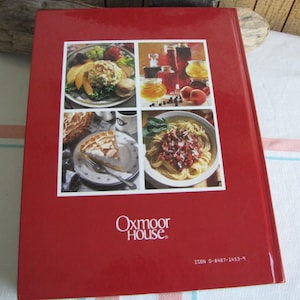 Puede incluir: Libro de cocina de tapa dura roja con el t&iacute;tulo "Oxmoor House" y un n&uacute;mero ISBN. La portada presenta cuatro fotos de comida: una ensalada, un postre, un plato de pasta y una selecci&oacute;n de frascos de conservas.