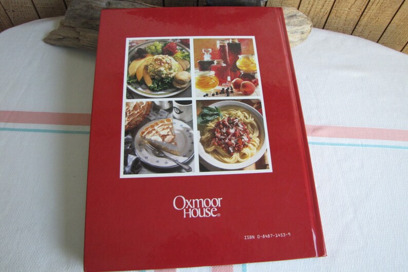 Puede incluir: Libro de cocina de tapa dura roja con el t&iacute;tulo "Oxmoor House" y un n&uacute;mero ISBN. La portada presenta cuatro fotos de comida: una ensalada, un postre, un plato de pasta y una selecci&oacute;n de frascos de conservas.