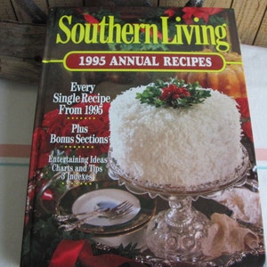 Puede incluir: Un libro titulado "Southern Living 1995 Annual Recipes" con un pastel blanco cubierto con coco rallado y una rama de acebo en un soporte de pastel plateado. La portada del libro presenta el texto "Every Single Recipe From 1995 Plus Bonus Sections Entertaining Ideas Charts and Tips 3 Indexes".