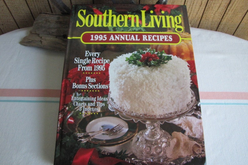 Puede incluir: Un libro titulado "Southern Living 1995 Annual Recipes" con un pastel blanco cubierto con coco rallado y una rama de acebo en un soporte de pastel plateado. La portada del libro presenta el texto "Every Single Recipe From 1995 Plus Bonus Sections Entertaining Ideas Charts and Tips 3 Indexes".