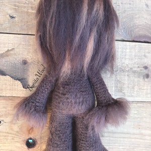 K&ouml;nnte beinhalten: Ein braunes und beigefarbenes gestricktes Pl&uuml;schtier mit langen Haaren. Das Spielzeug steht auf einer Holzoberfl&auml;che. Der Text "Bonita Wool" ist auf dem Spielzeug sichtbar.
