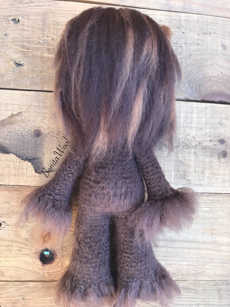 K&ouml;nnte beinhalten: Ein braunes und beigefarbenes gestricktes Pl&uuml;schtier mit langen Haaren. Das Spielzeug steht auf einer Holzoberfl&auml;che. Der Text "Bonita Wool" ist auf dem Spielzeug sichtbar.