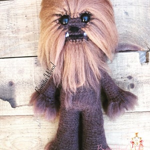 K&ouml;nnte beinhalten: Ein braunes, geh&auml;keltes Chewbacca-Pl&uuml;schtier mit schwarzen Augen und einem wei&szlig;en Bart. Das Spielzeug steht auf einer Holzoberfl&auml;che. Der Text "Bonita Wool!" ist auf dem Spielzeug geschrieben.
