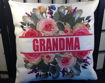May include: White pillow with a floral design featuring pink and yellow roses, green leaves, and purple flowers. The pillow has a pink banner with the word "GRANDMA" printed in white.