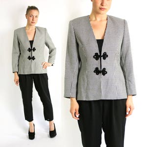 Peut inclure: Un blazer à carreaux noir et blanc avec des fermetures décoratives noires. Le blazer est associé à un pantalon noir et des chaussures noires. L'ensemble est présenté sur fond blanc.