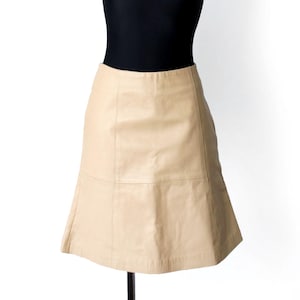 Op de afbeelding: Beige A-lijn rok op een zwarte mannequin. De rok heeft een subtiele glans en een klassiek ontwerp, geschikt voor diverse gelegenheden. De mannequin staat tegen een effen witte achtergrond.