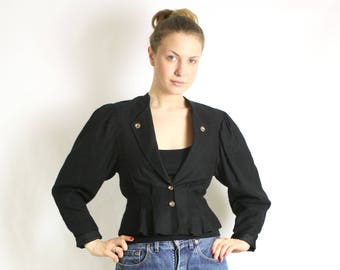 Puede incluir: Una chaqueta negra corta con botones dorados y un dobladillo con volantes, combinada con jeans de mezclilla azul y zapatos negros de tacón.
