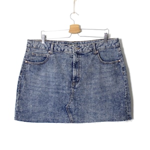 Op de afbeelding: Een lichtblauwe denim minirok met een distressed look. De rok heeft twee voorzakken en een knoop- en ritssluiting.