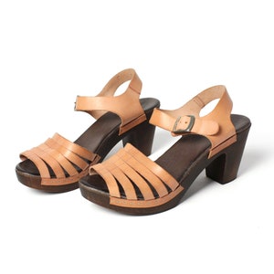 May include: A pair of tan leather heeled sandals with a woven strap design. The sandals have a closed toe and an open heel.