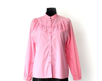 May include: A pink long-sleeved button-up shirt with a ruffled collar and a stand-up collar.