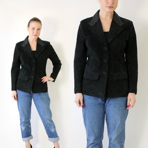 May include: A black suede jacket with a notched collar and button fastening. The jacket is being worn by a person with blue jeans and black heels.
