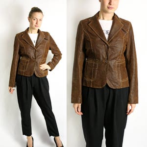 Peut inclure: Une veste en cuir marron avec des détails de couture et une fermeture à bouton. La veste a une silhouette ajustée et un col.